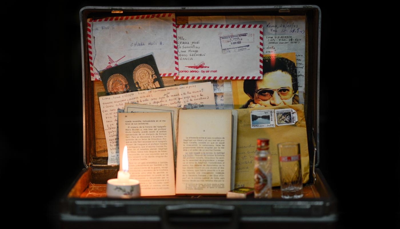 An open suitcase holding various papers and a lit candle