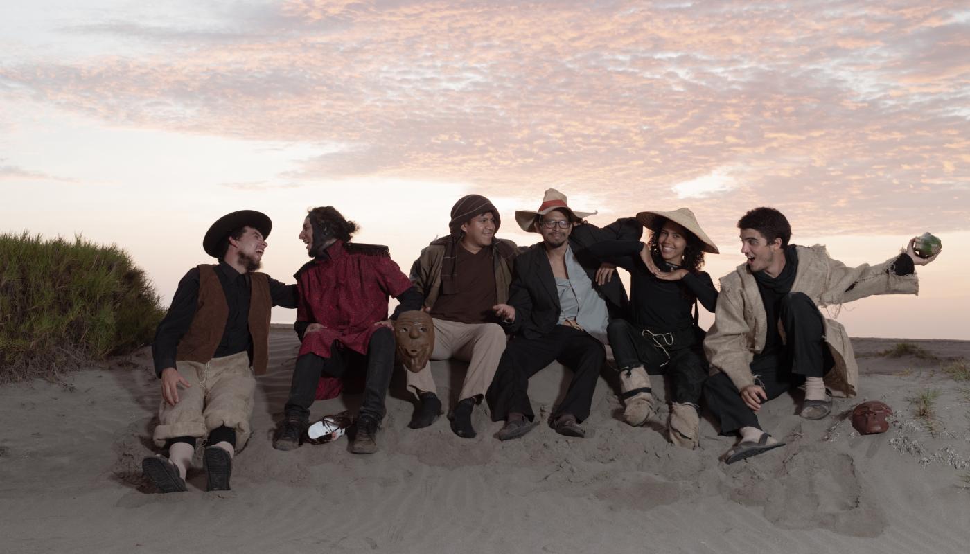 Group of musicians, sitting on a sand dune in front of a sunset