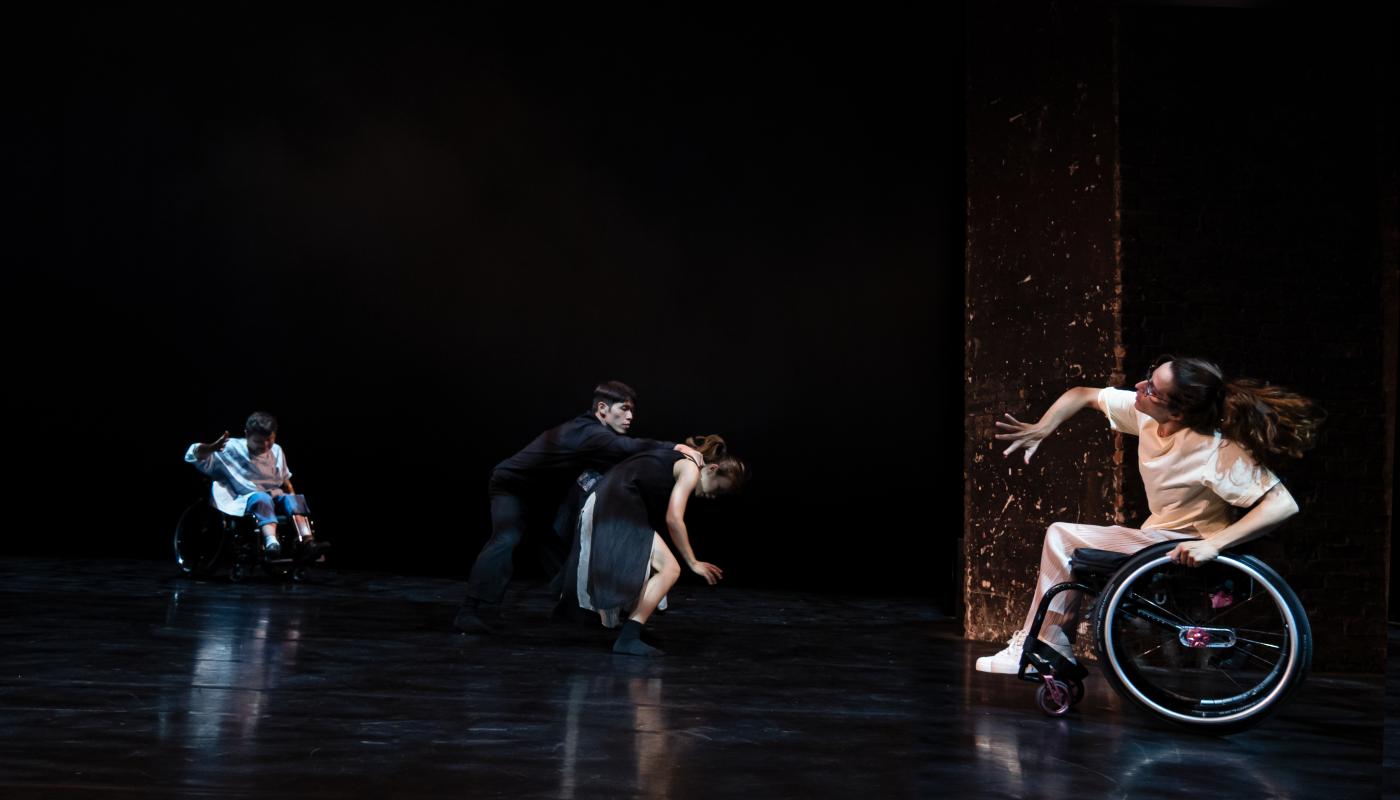 Four dancers, two able-bodied and two in wheelchairs, perform on a large open stage.
