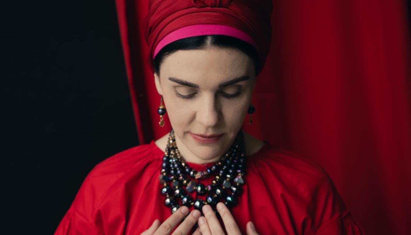 A woman in traditional Ukrainian clothing, looking down with her hands on her chest