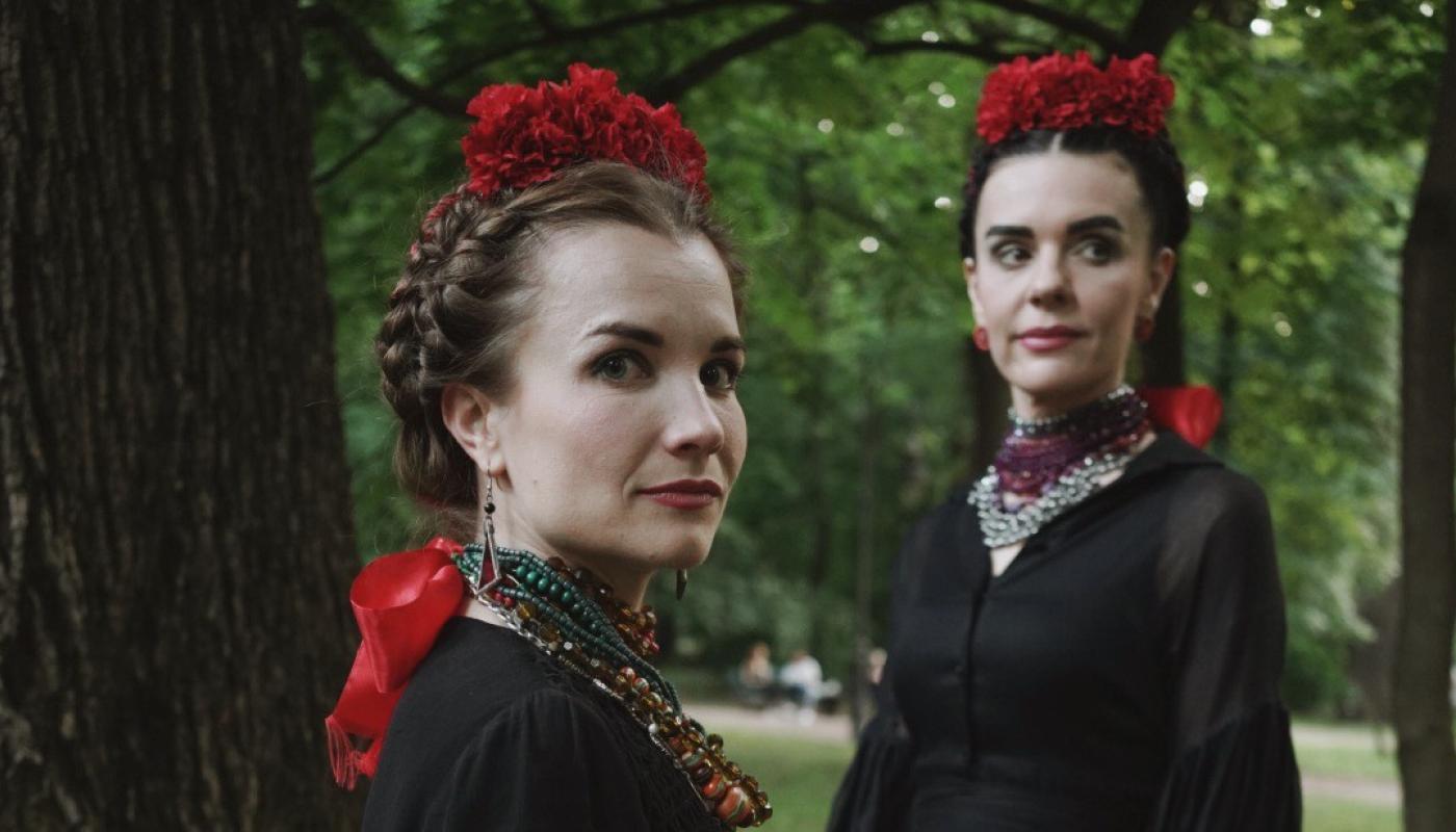 Two women in traditional Ukranian clothing standing in a forest looking at the camera