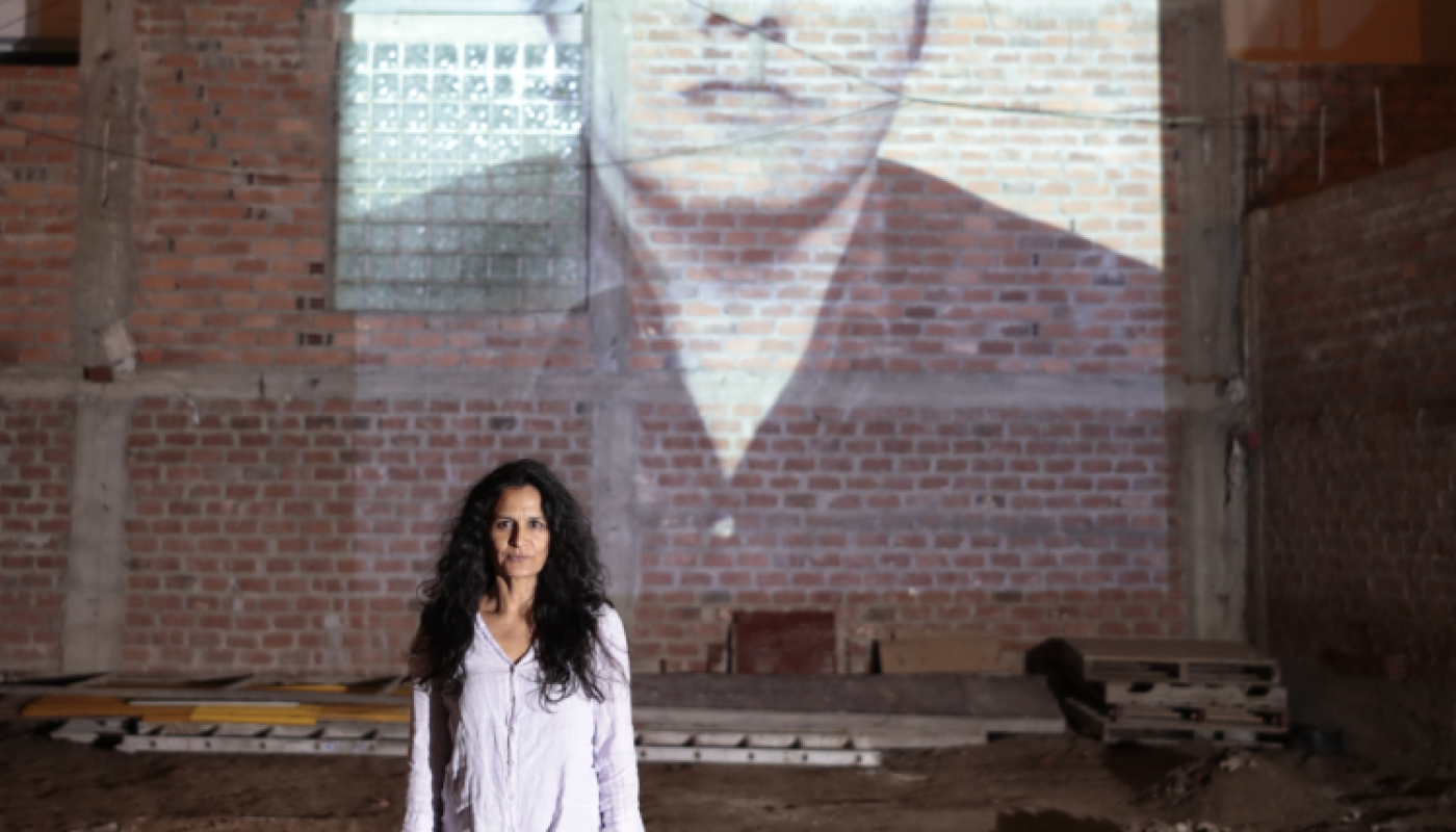 Woman standing in front of a brick wall, with an image of a man projected onto it