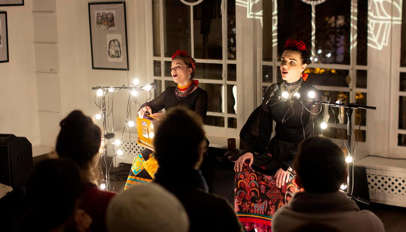 Two women perform in front of a crowd, lit by Christmas lights