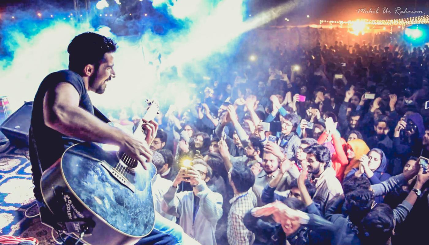 A man plays a guitar in front of a crowed with their arms raised