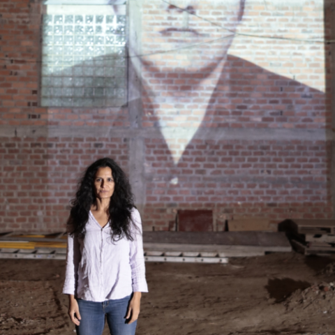 Fílmico, photo courtesy of Claudia Zignago (2) Woman standing in front of a brick wall, with an image of a man projected onto it