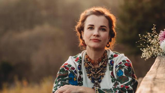 Maria of Kurbasy, photo by Liuba Chornenjka A woman sitting on a bench with her knees up close to her chest, backlit by the sun