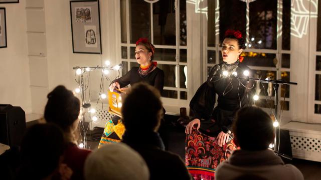 Kurbasy, courtesy of the band Two women perform in front of a crowd, lit by Christmas lights