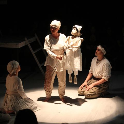 A group of people, all wearing white, sitting around someone holding a small puppet