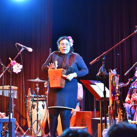The Peruvian band Lundu performs on stage led by their frontwoman playing the plays a cajita, an Afro-Peruvian percussion instrument